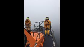 2 crew members standing on the bow of the Lifeboat faced with think fog