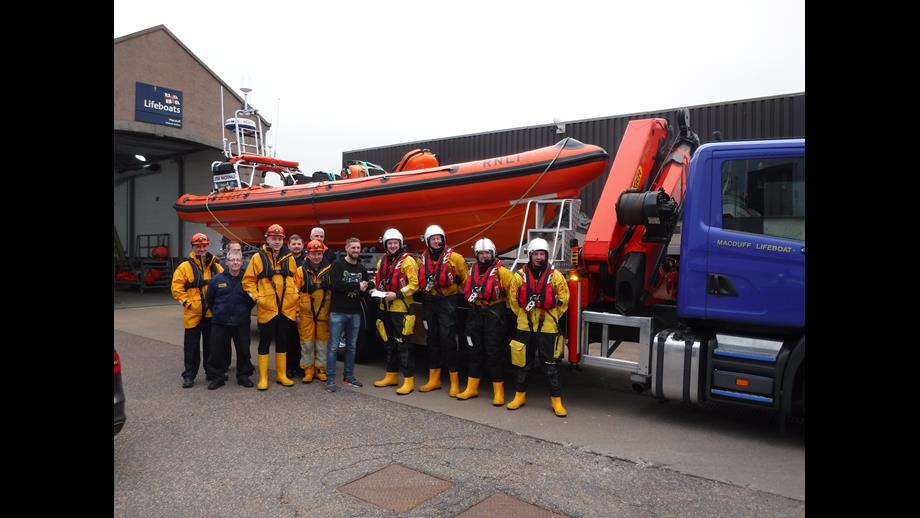 RNLI crew in drysuits standing in front of RNLI Macduff lifeboat B-804 Lydia Macdonald with local footballer Graeme Watt