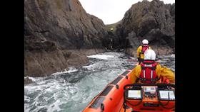 picture from the back of the lifeboat looking forwards, two crew members look towards cliff face where a thirds RNLI crew member is with police, ambulance and the casualty