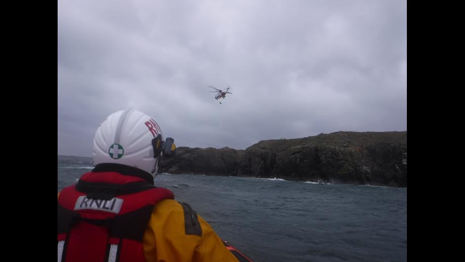 Coastguard helicopter Rescue 951 winching the casualty to safety with RNLI crew member in the foreground