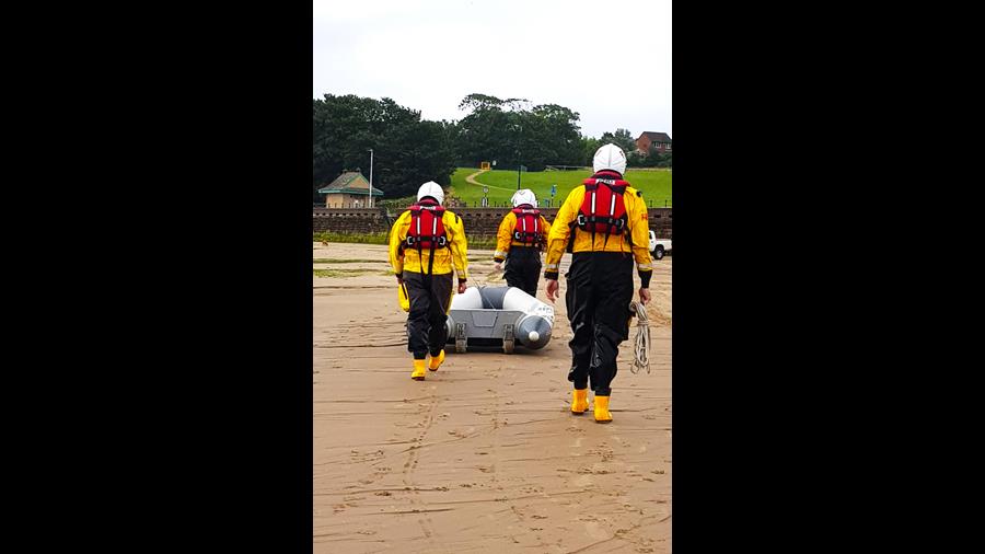 The backs of three RNLI shore crew as they pull the dinghy up the sand 