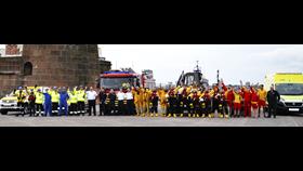 Line up of emergency teams in front of their service vehicles with Fort Perch Rock as a backdrop