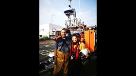 Mike and Lucy stand side by side in front of the lifeboat on its carriage 