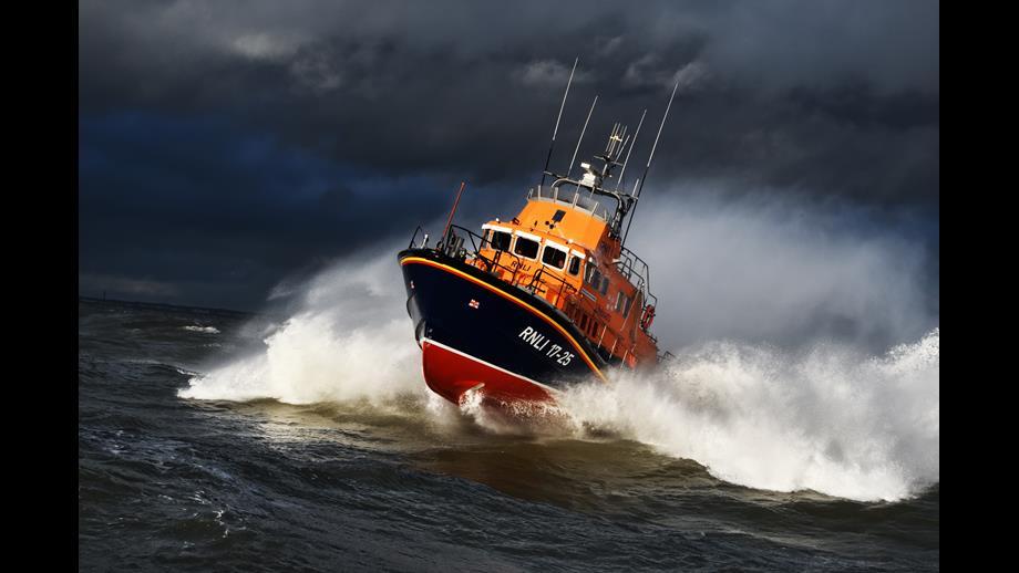 armouth RNLI's Severn class lifeboat crashing through waves with dark clouds above it