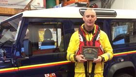RNLI crew member proudly holding Grandad's Gold Medal in front of RNLI branded Land Drover