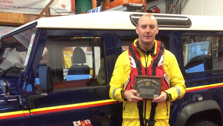 RNLI crew member proudly holding Grandad's Gold Medal in front of RNLI branded Land Drover
