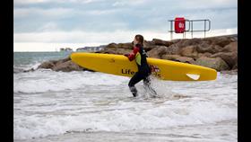 Female lifguard is running into the sea with a rescue board