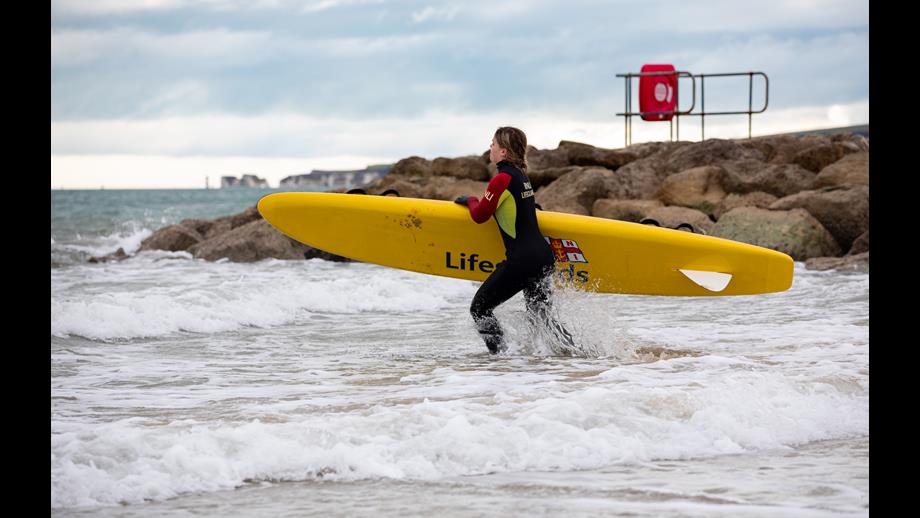 Female lifguard is running into the sea with a rescue board