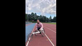 A man in a pink shirt sits in a bicycle wheelchair on an athletics track.