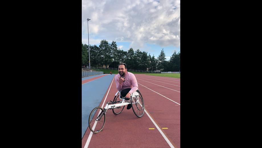 A man in a pink shirt sits in a bicycle wheelchair on an athletics track.
