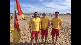 Three lifeguards stand together on the beach in the RNLI uniform. Luke Dixon is on the right of the three.