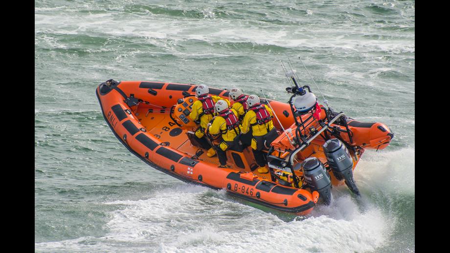 the orange inshore lifeboat speeds through the water with four crew onboard
