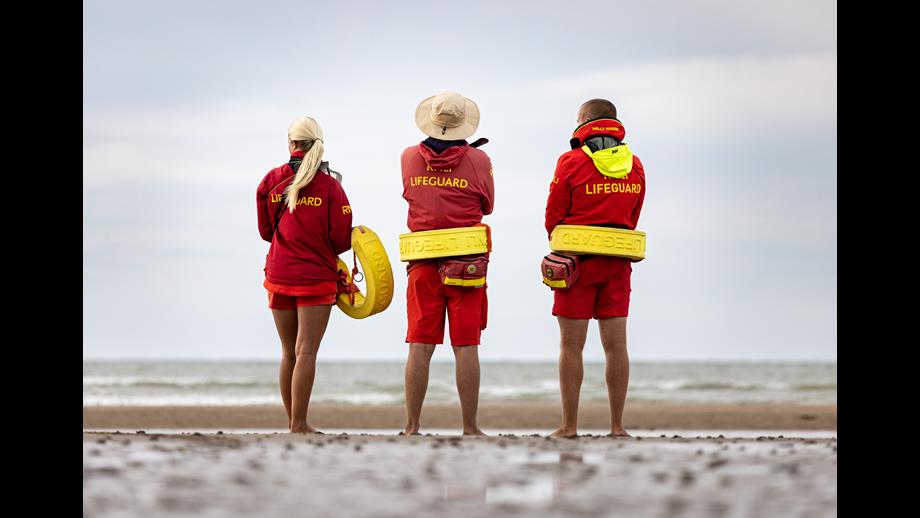Three RNLI Lifeguards patrolling the beach near the water holding rescue tubes