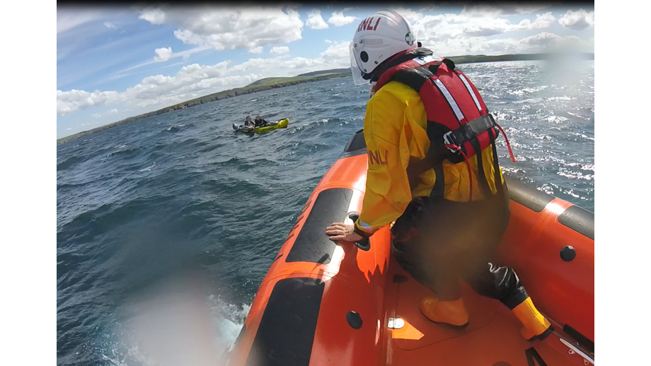 Volunteer lifeboat crew member Rob Smith at the bow of lifeboat B-804 with an inflatable kayak with two people in it, just in front of him