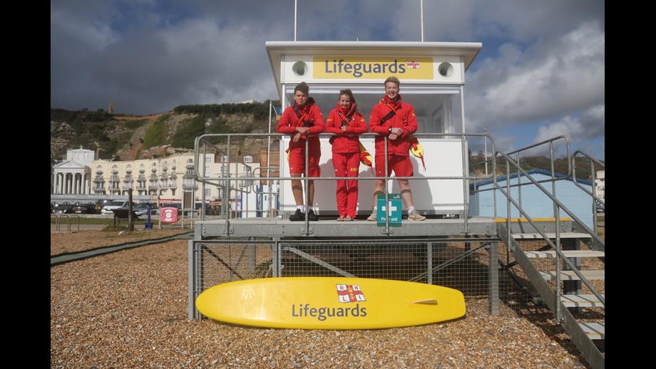 Three RNLI Lifeguards in front of the lifeguarding hut in Hastings 