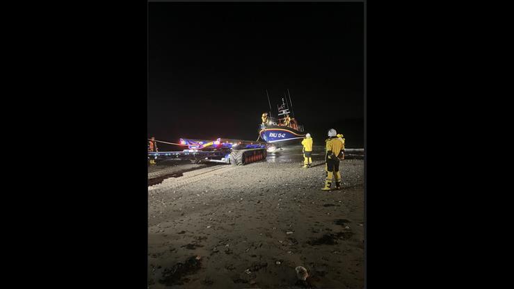 Lifeboat and shore crew stood on the sand, the lifeboat is in the water ready to be pulled back onto the trailer