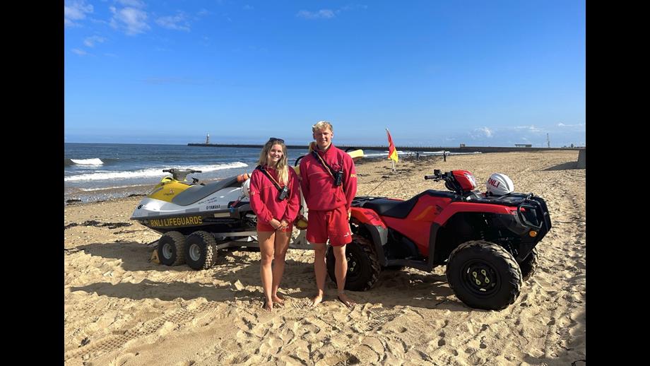 RNLI lifeguards Abby Cass (left) and Chris Trotter (right) in front of an RNLI rescue watercraft