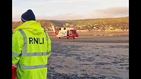 RNLI volunteer in foreground and Coastguard helicopter in background on beach
