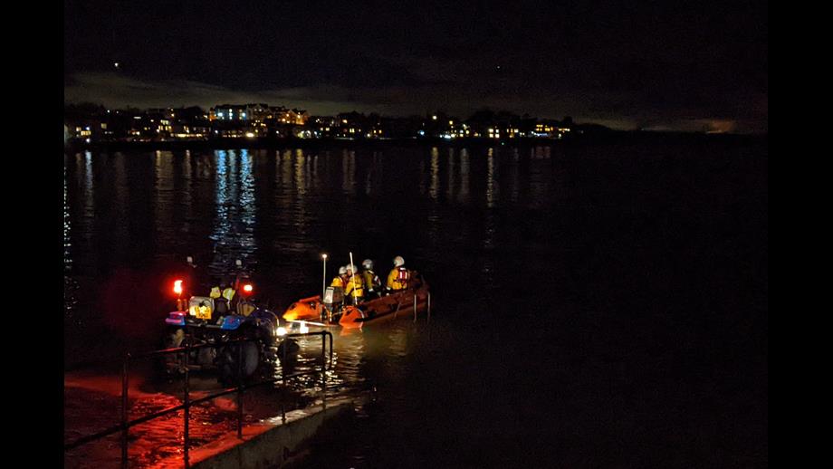 North Berwick RNLI launching at night, at high tide with tractor and lifeboat driving off trailer, town lights in the background