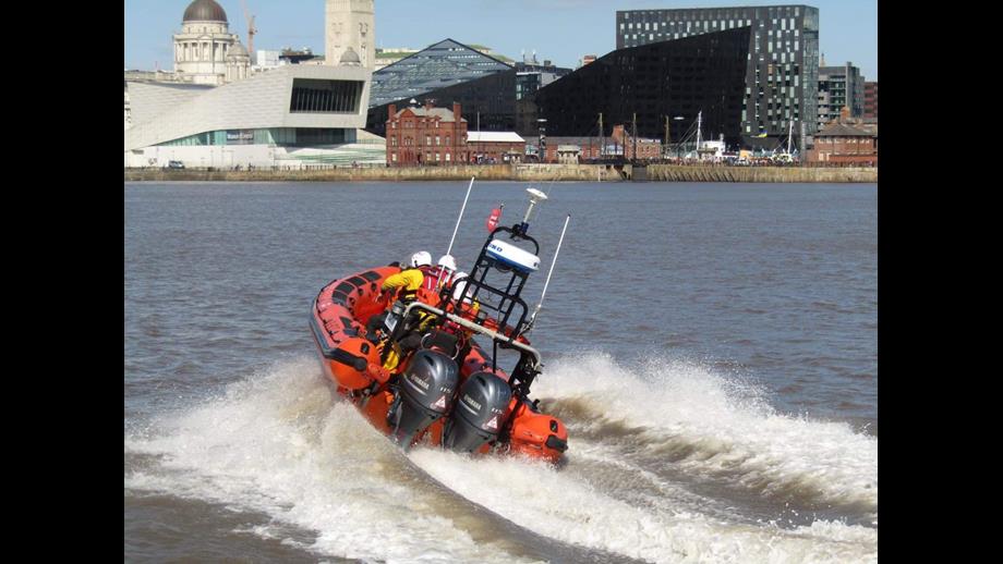 The River Mersey dominates the image, with New Brighton lifeboat trailing wake as it speeds off toward the Liverpool skyline, which can be seen in the background.
