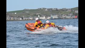 Two, yellow-clad volunteers, wearing white helmets operating a small RIB in the harbour