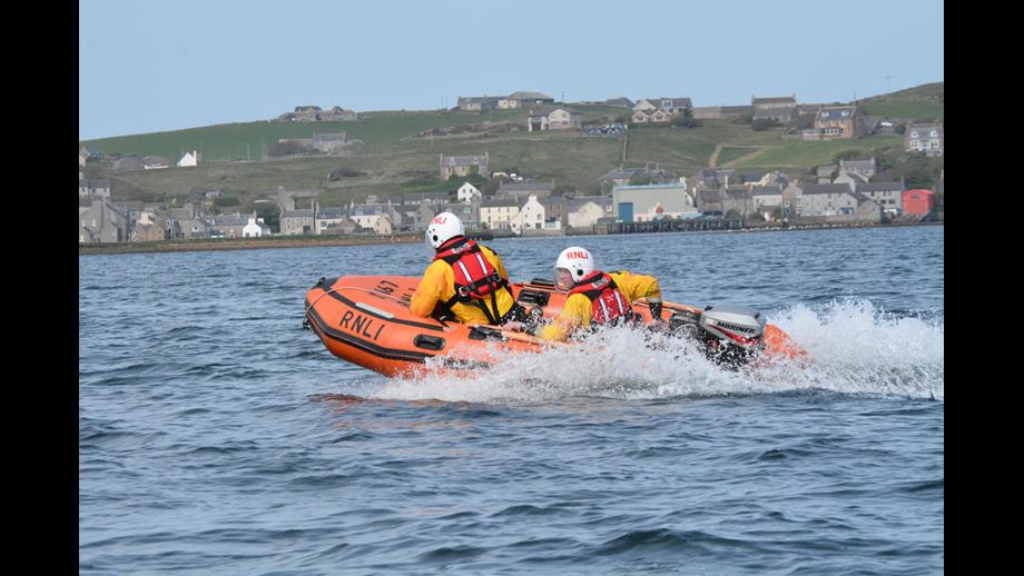 Two, yellow-clad volunteers, wearing white helmets operating a small RIB in the harbour