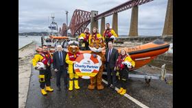 RNLI crew members can be seen at Queensferry RNLI Lifeboat Station in crew kit and with the lifeboat, alongside Scotmid representatives