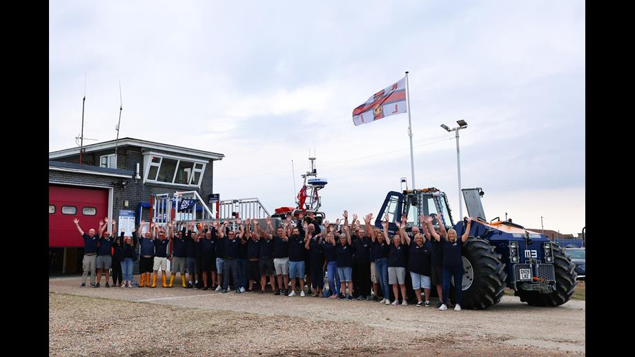 A group of 50 volunteers stand infront the the lifeboat and tractor and lift their arms in celebration at Littlestone RNLI