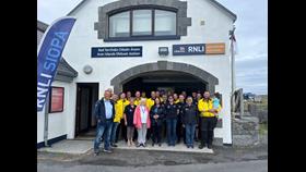 A group of 23 crew and volunteers standing outside the Aran Islands station with a feather banner with RNLI Siopa on left hand side.