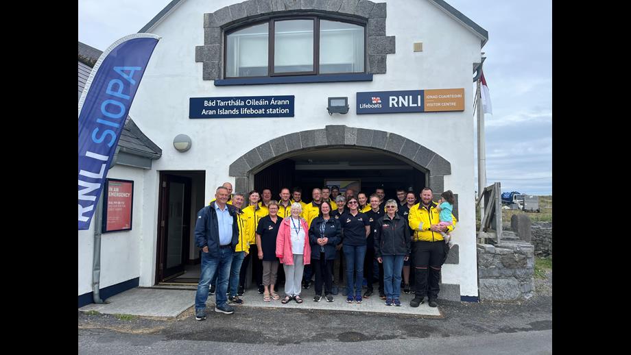 A group of 23 crew and volunteers standing outside the Aran Islands station with a feather banner with RNLI Siopa on left hand side.