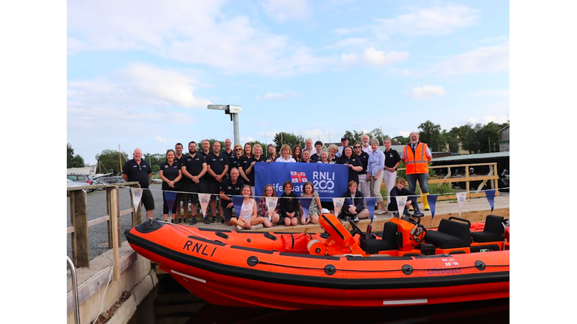 Volunteers and their family stand on the pontoon above and behind the lifeboat, which is dressed in RNLI200 bunting for the One Moment One Crew photograph.