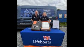 Peter and Niamh hold up the RNLI scroll which they have just signed. They are stganding ion front ofg the RNLI van which is carrying the scroll to stations thoughout the UK and Ireland