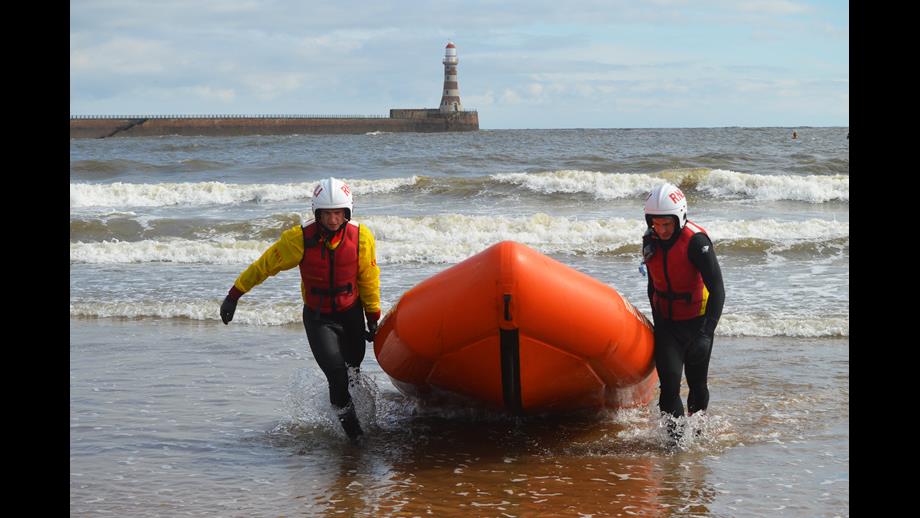 Two lifeguards in training dragging an inshore lifeboat out the water. 