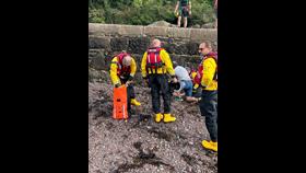 RNLI Jersey crew, kitted up in their dry suits, provide casualty care to an injured boy, who had fallen off the slip, to the side of the slip at Little St Catherine's