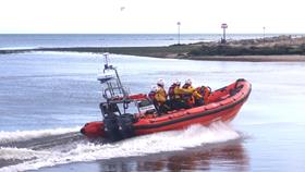 An RNLI orange rib with four crew speeds through the water.