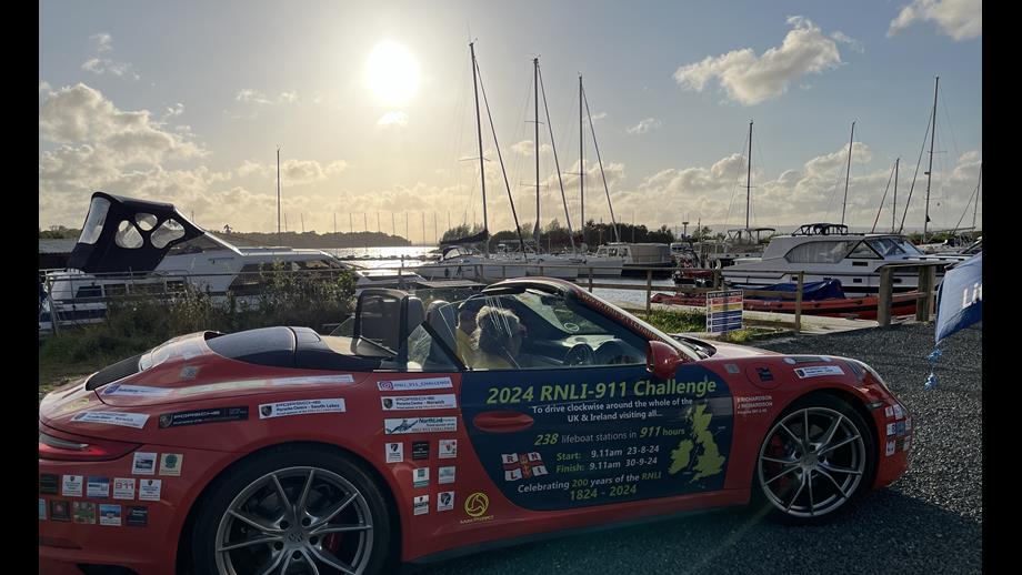 Porsche 911 challenge stops at Lough Derg RNLI James and Belinda Richardson having jut arrived in their Porsche 911 at Lough Derg RNLI, the lifeboat is moored up behind them, and there is a buttery sunset on the horizon