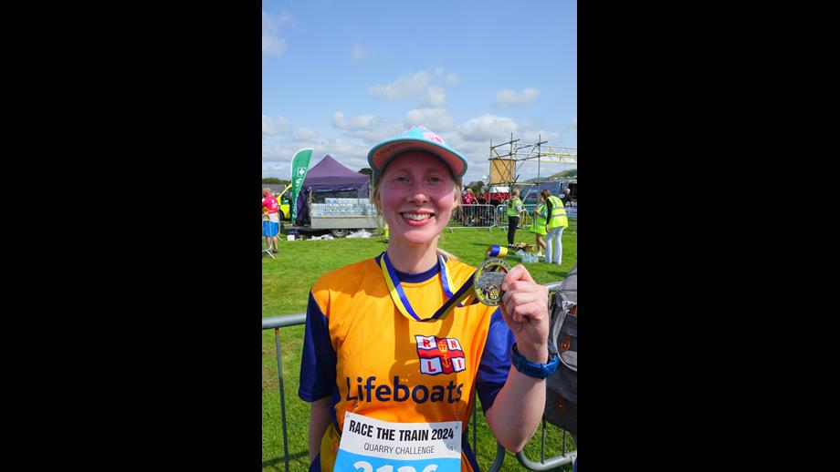 Louise is standing, wearing her Lifeboats T shirt and holding up her medal