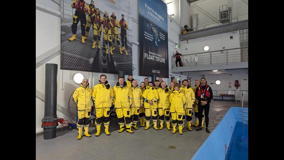 Group of people in yellow uniform stood together next to a pool of water