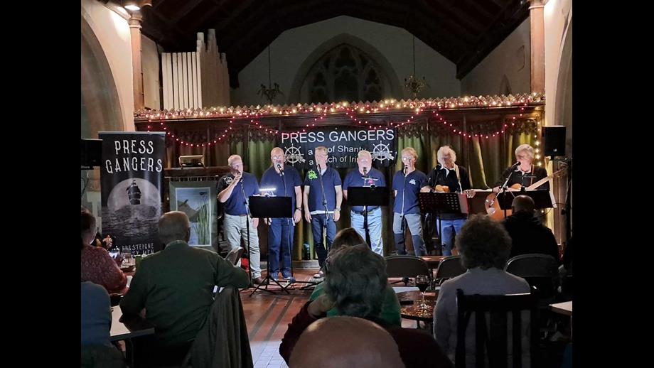 Press Gangers on stage in a church performing with fairy lights in the background.