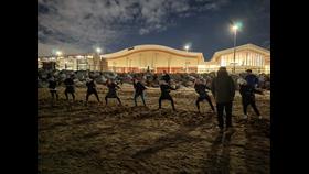 A night time shot, on New Brighton beach. Floral Pavilion theatre visible in the background, whilst on the beach in the foreground, a team of volunteers from New Brighton RNLI hold and pull hard on a long rope. Others stand nearby watching.