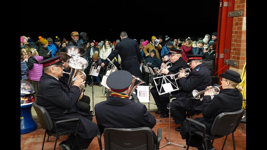 Seated band members in boathouse entrance with crowd of people outside