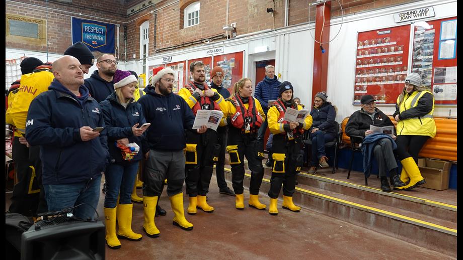 Lifeboat crew members in yellow wellies and drysuits with lifejackets in the boathouse