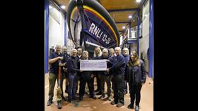 A group of men and women holding a large cheque in front of a Lifeboat