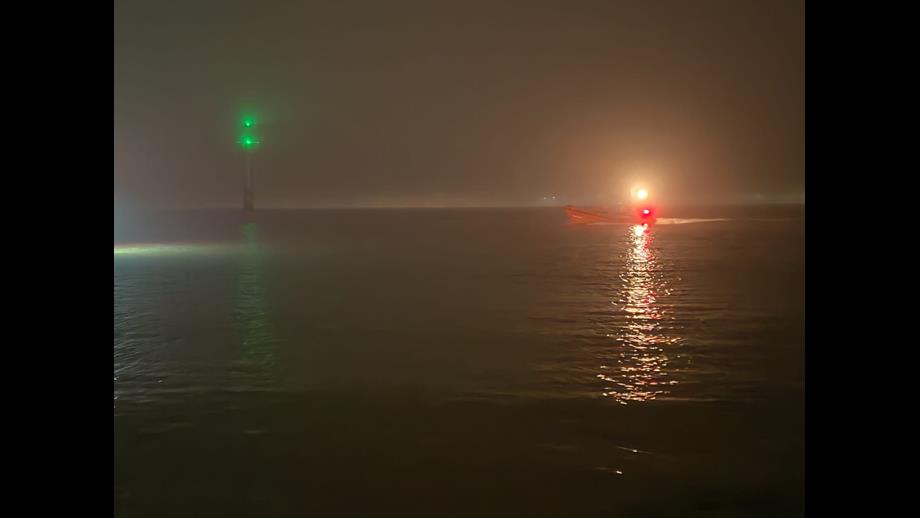 A slightly unclear photo of the river Mersey from the shore. A groyne marker can be seen to the left of the image, with illuminated green top. The lifeboat is off to the right, lit by its navigation lights. A very foggy night.