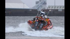 The rear of New Brighton RNLI's Atlantic-85 lifeboat can be seen causing wake on the River Mersey as it heads away from camera, launching.

