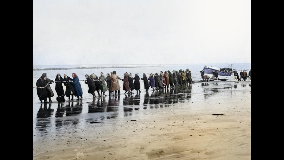 A colourised image of a line of women hauling in a lifeboat.
