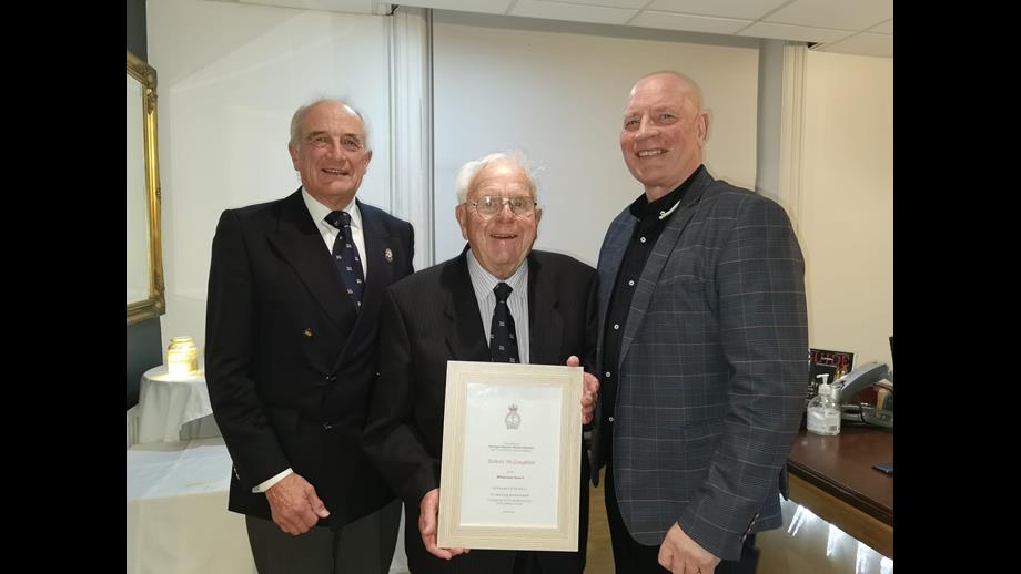 Three men in suits. One in middle holding certificate