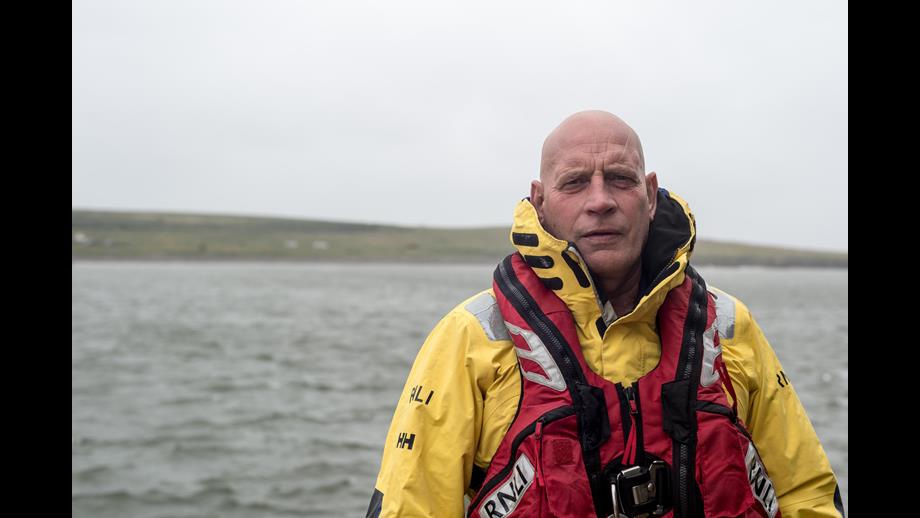 Man in RNLI gear - yellow jacket and red lifejacket - in front of sea