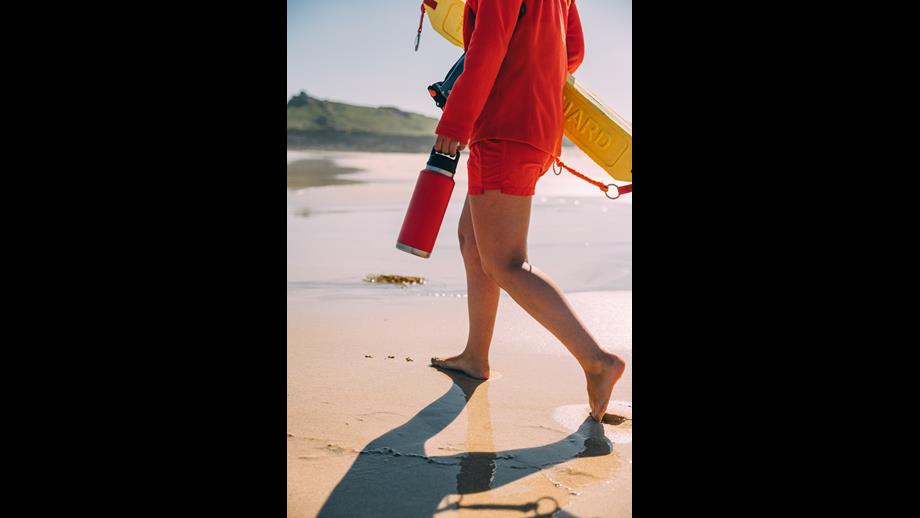 RNLI lifeguard walking along the shore with a Yeti bottle 