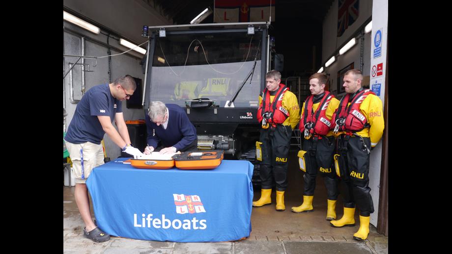 George Craig signing the 200th Anniversary scroll in front of the lifeboat tractor with 3 other volunteer crew stood to the side